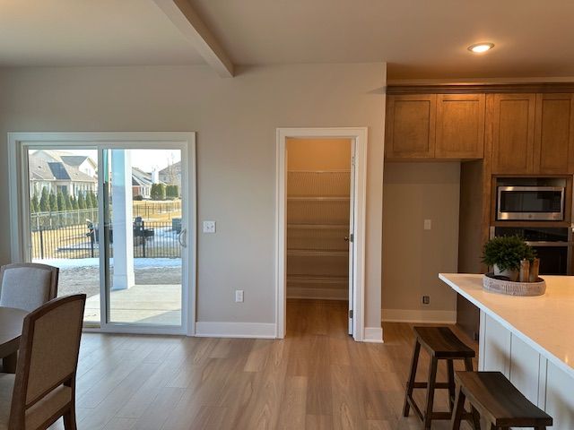 kitchen with brown cabinetry, light wood finished floors, beam ceiling, light countertops, and stainless steel microwave