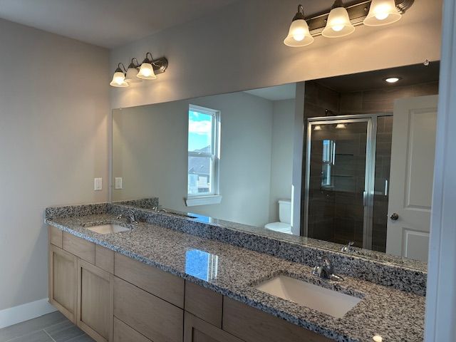 bathroom with a sink, toilet, double vanity, and a shower stall