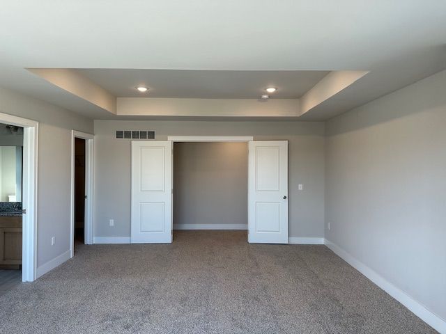 unfurnished bedroom featuring carpet, a tray ceiling, baseboards, and visible vents