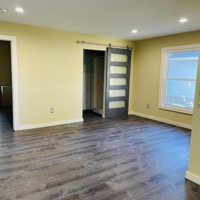 unfurnished bedroom with dark hardwood / wood-style floors, a barn door, and a closet