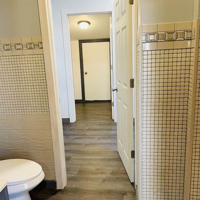 bathroom with wood-type flooring, toilet, and tile walls