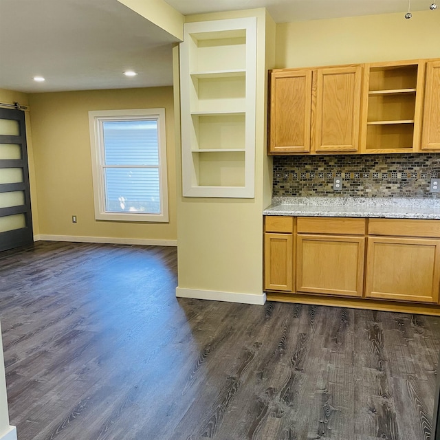 kitchen with light stone countertops, built in features, dark hardwood / wood-style flooring, and decorative backsplash