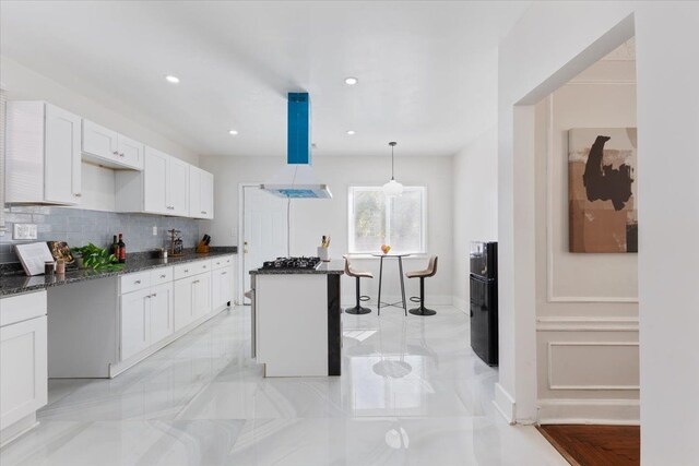 kitchen with white cabinetry, a center island, tasteful backsplash, dark stone counters, and decorative light fixtures