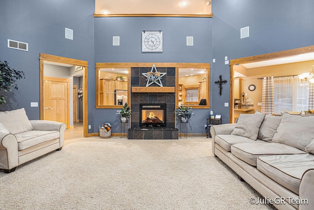 carpeted living room featuring a tile fireplace, a towering ceiling, and a chandelier