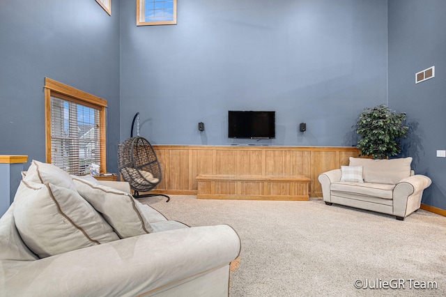 carpeted living room with a high ceiling and wooden walls