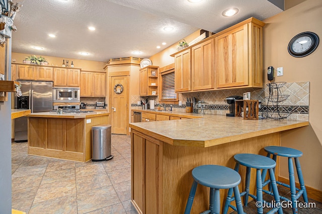 kitchen featuring kitchen peninsula, appliances with stainless steel finishes, decorative backsplash, and a breakfast bar area