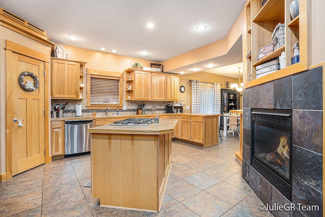 kitchen with decorative backsplash, light brown cabinetry, appliances with stainless steel finishes, a tile fireplace, and a kitchen island