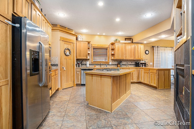 kitchen featuring light brown cabinets, decorative backsplash, a textured ceiling, a kitchen island, and stainless steel appliances