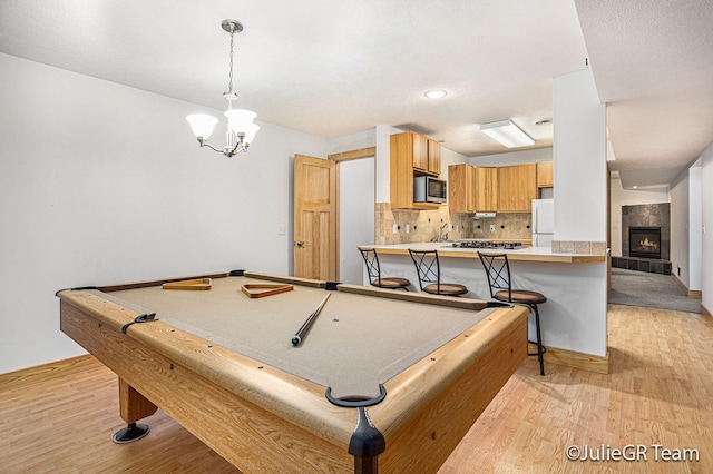 game room with a tile fireplace, an inviting chandelier, light hardwood / wood-style floors, and pool table