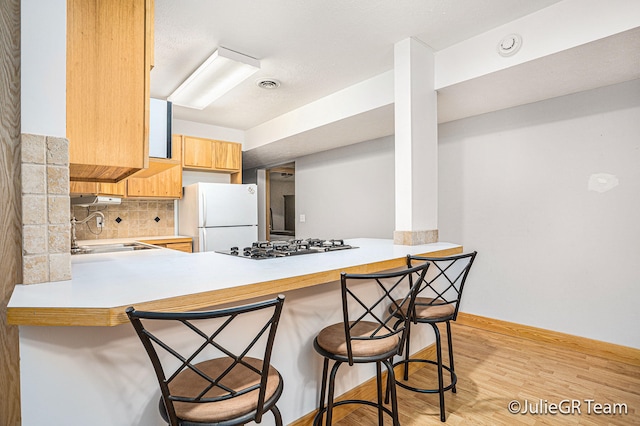 kitchen featuring sink, tasteful backsplash, light hardwood / wood-style flooring, white refrigerator, and kitchen peninsula