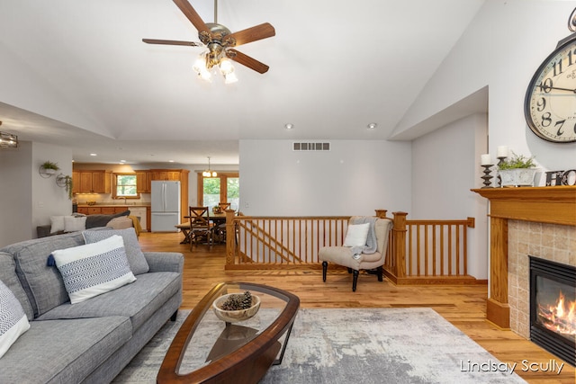 living room featuring ceiling fan, a fireplace, lofted ceiling, and light wood-type flooring