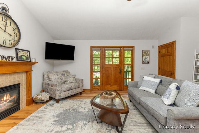 living room featuring a tiled fireplace, hardwood / wood-style floors, and vaulted ceiling