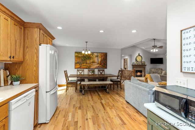 kitchen featuring white appliances, ceiling fan with notable chandelier, hanging light fixtures, vaulted ceiling, and light wood-type flooring