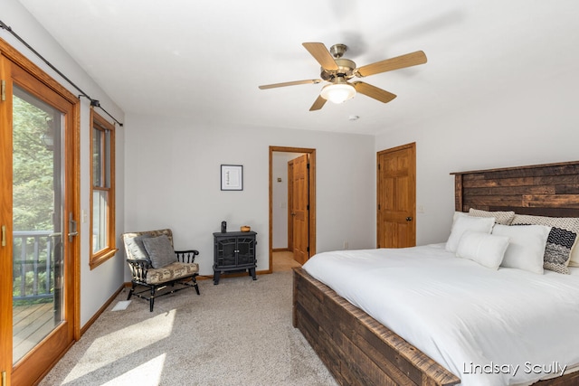 carpeted bedroom with ceiling fan, a wood stove, and access to outside