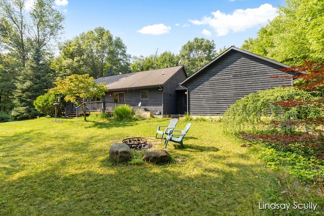 rear view of house with a lawn, a deck, and an outdoor fire pit