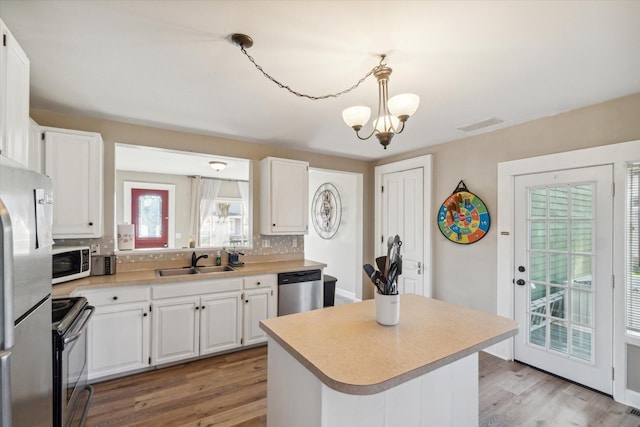 kitchen featuring white cabinets, hanging light fixtures, sink, light wood-type flooring, and appliances with stainless steel finishes