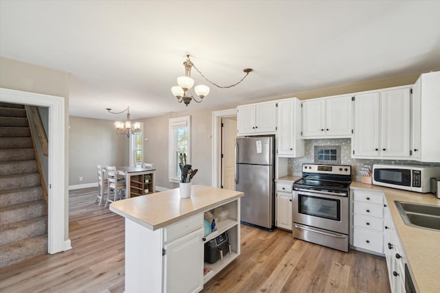 kitchen featuring light hardwood / wood-style floors, white cabinetry, hanging light fixtures, and appliances with stainless steel finishes