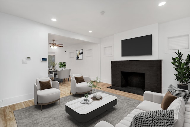 living room with ceiling fan, wood-type flooring, and a brick fireplace