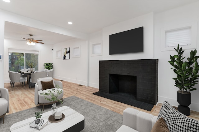 living room with light wood-type flooring, a brick fireplace, and ceiling fan