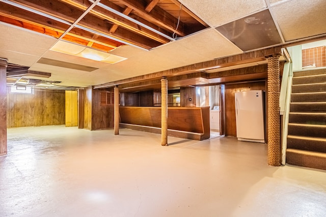 basement with white fridge, washer / clothes dryer, and wood walls