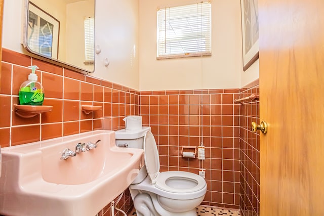 bathroom with toilet, sink, and tile walls