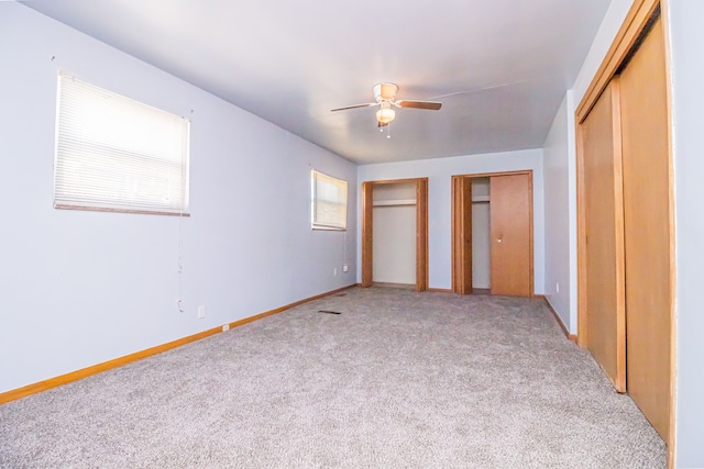 unfurnished bedroom with multiple closets, ceiling fan, and light carpet