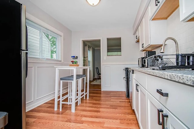 kitchen with tasteful backsplash, stainless steel fridge, white cabinets, and light wood-type flooring