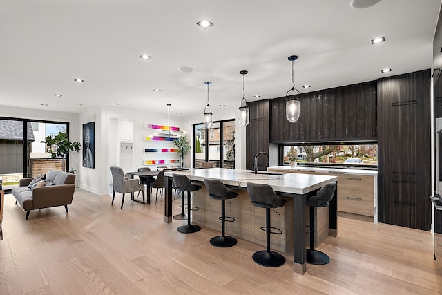 kitchen with a breakfast bar area, a wealth of natural light, light hardwood / wood-style flooring, and an island with sink