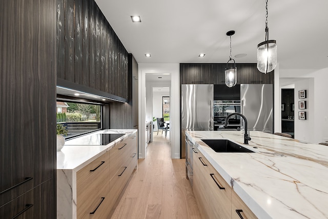 kitchen featuring pendant lighting, sink, stainless steel fridge, light stone countertops, and light wood-type flooring