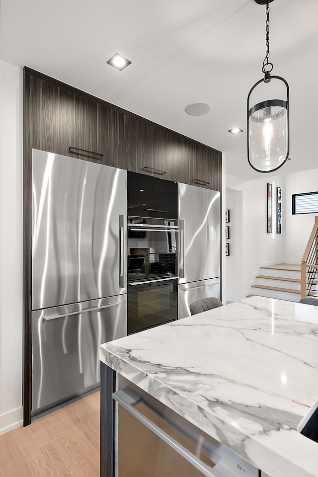 kitchen with stainless steel refrigerator, light stone counters, light hardwood / wood-style flooring, and dark brown cabinets