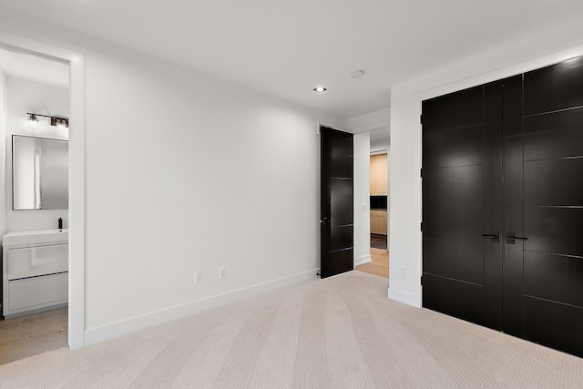 unfurnished bedroom featuring a closet, light colored carpet, and ensuite bath