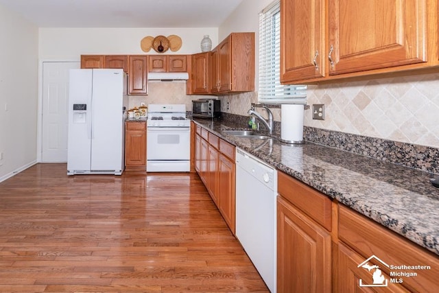 kitchen featuring white appliances, light hardwood / wood-style flooring, dark stone counters, and sink