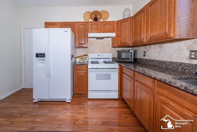 kitchen with white appliances, dark hardwood / wood-style flooring, dark stone counters, and tasteful backsplash