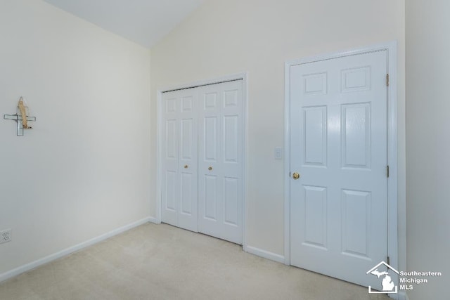 unfurnished bedroom featuring a closet, light carpet, and lofted ceiling