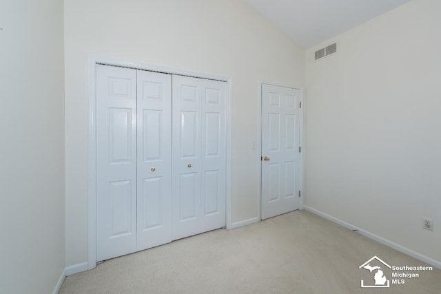 unfurnished bedroom featuring high vaulted ceiling, a closet, and light carpet