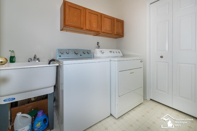 clothes washing area with sink, washing machine and dryer, and cabinets