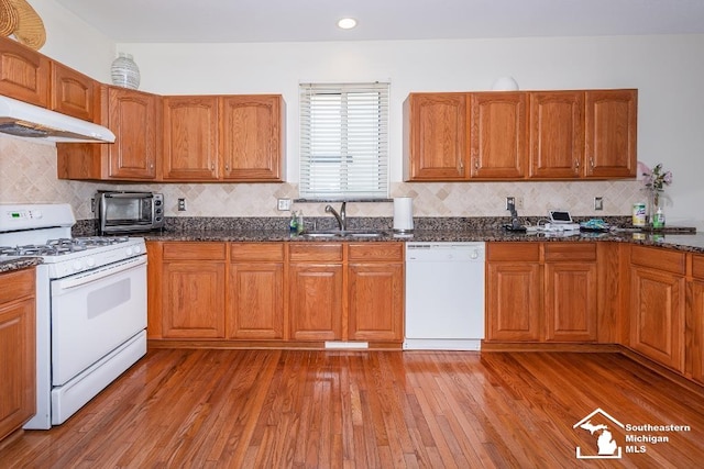 kitchen featuring white appliances, tasteful backsplash, light wood-type flooring, dark stone counters, and sink