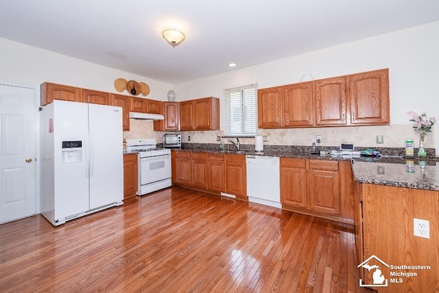 kitchen with white appliances, dark stone counters, decorative backsplash, and hardwood / wood-style flooring