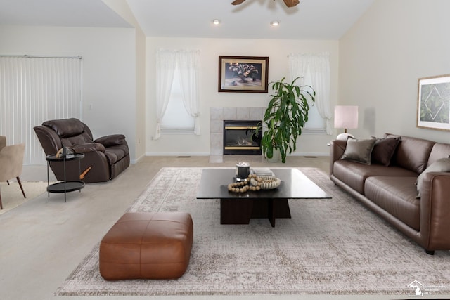 living room with a tiled fireplace, ceiling fan, and light colored carpet