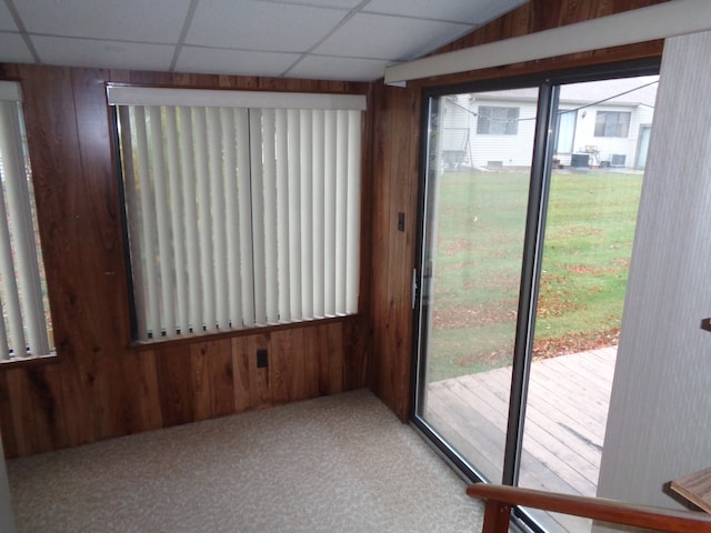 interior space with carpet flooring, a drop ceiling, and wood walls