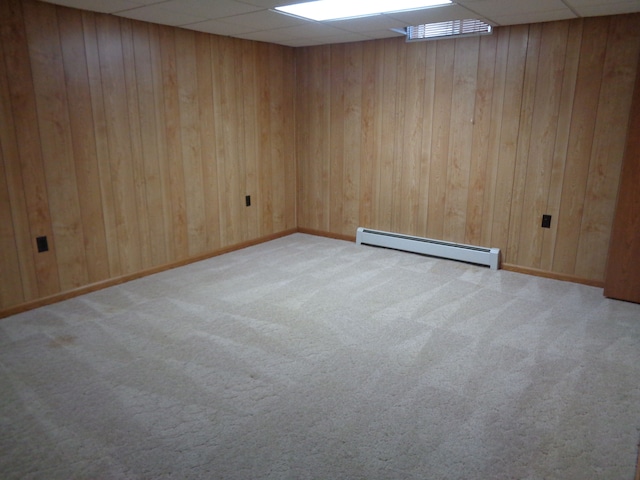 carpeted spare room with a paneled ceiling, wooden walls, and a baseboard radiator