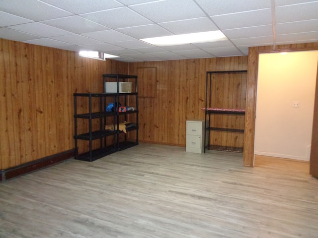 basement featuring a paneled ceiling, light hardwood / wood-style flooring, and wooden walls