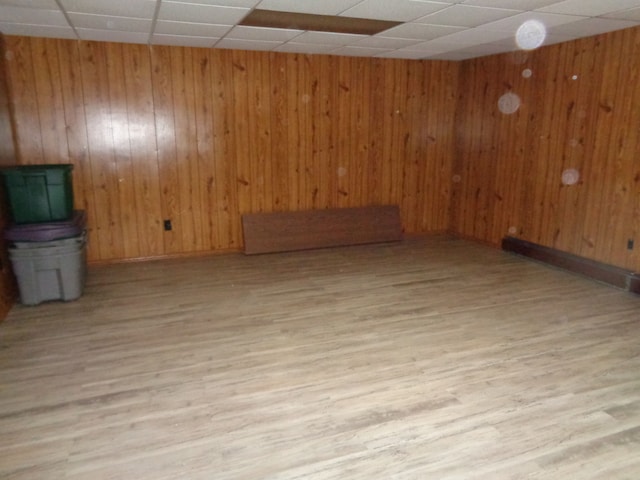 unfurnished room with wood walls, a drop ceiling, and light hardwood / wood-style floors