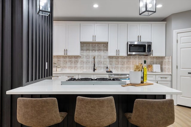 kitchen with tasteful backsplash, white cabinetry, hanging light fixtures, and stainless steel appliances