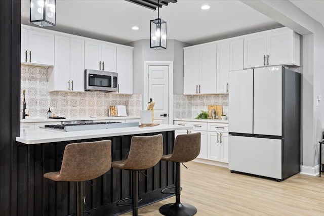 kitchen with stainless steel appliances, tasteful backsplash, decorative light fixtures, white cabinets, and light wood-type flooring