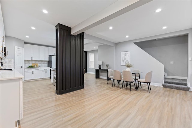 kitchen featuring sink, decorative backsplash, light wood-type flooring, stainless steel range oven, and white cabinetry