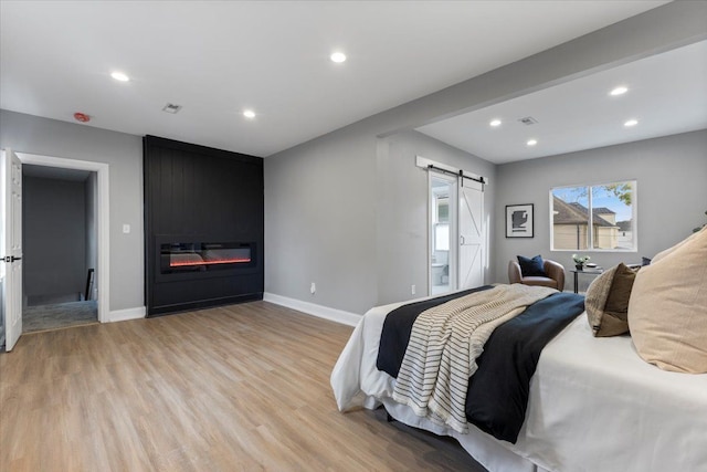 bedroom with a large fireplace, a barn door, and light hardwood / wood-style floors