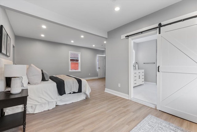 bedroom featuring a barn door, ensuite bathroom, and light hardwood / wood-style flooring