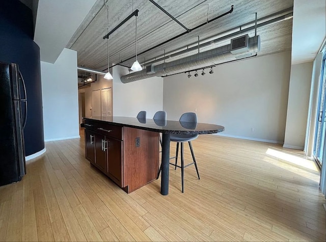 kitchen featuring black refrigerator, hanging light fixtures, light hardwood / wood-style flooring, a kitchen island, and a kitchen bar