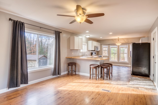 kitchen with kitchen peninsula, appliances with stainless steel finishes, light hardwood / wood-style floors, white cabinetry, and a breakfast bar area